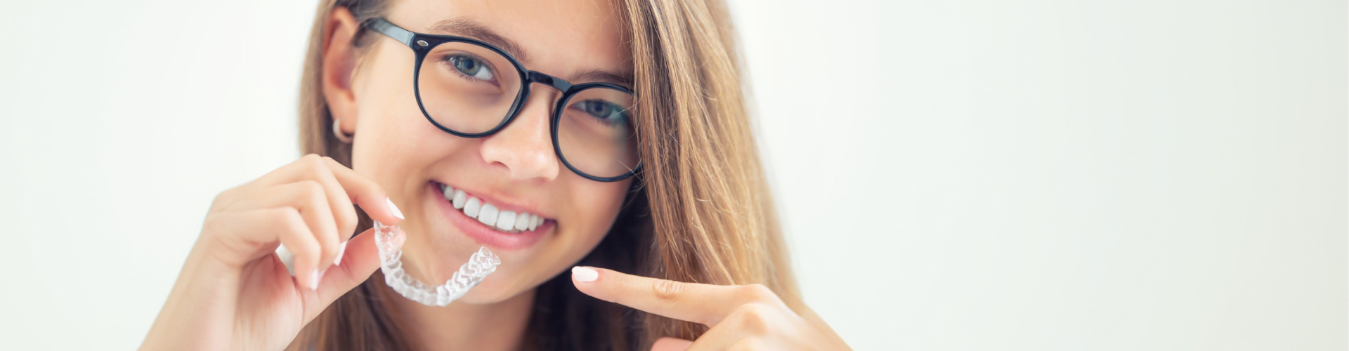 Smiling girl wearing glasses holding clear aligner.